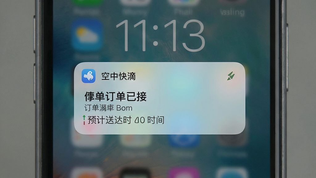 手机锁屏界面弹出“空中快滴”通知卡片,显示订单已接单和预计送达时间,布局为手机居中,风格为写实UI风格,细节包括通知图标和文字内容,画质清晰,干净,无多余元素